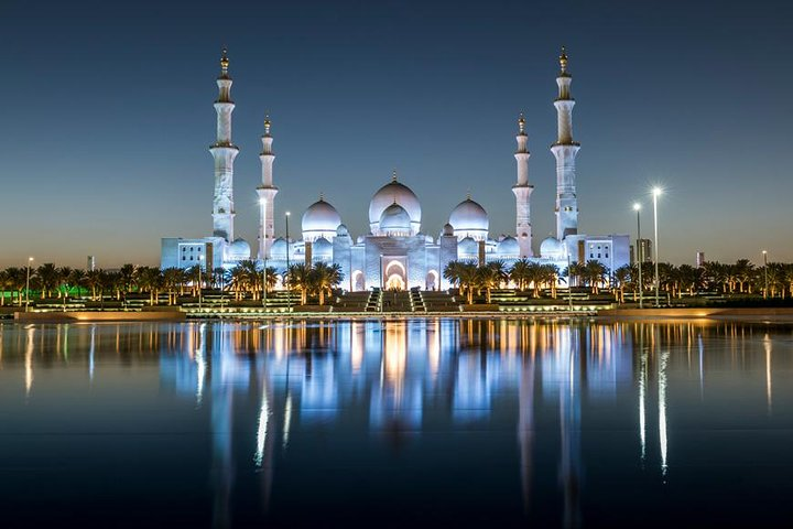 Experience the stunning Sheikh Zayed Grand Mosque illuminated at twilight reflecting beautifully in the serene waters showcasing Abu Dhabi's architectural marvels and rich culture.